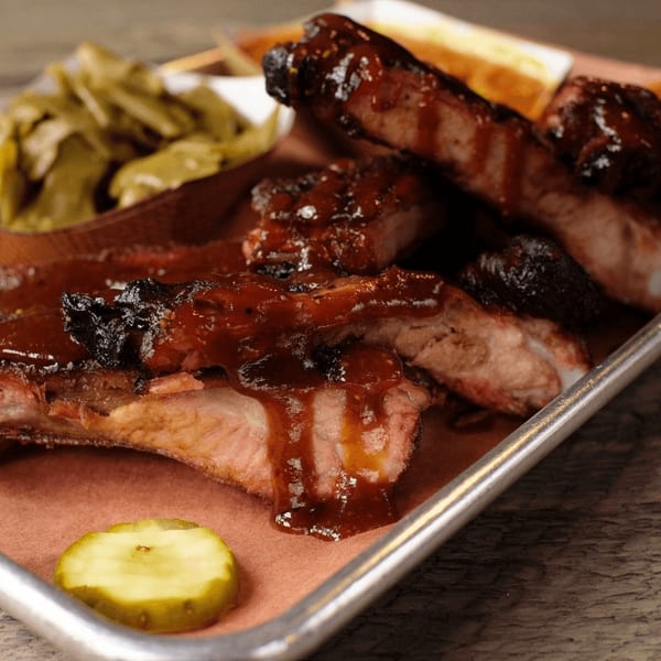 Fire It Up BBQ ribs with sauce, a pickle slice, and green beans on a metal tray.