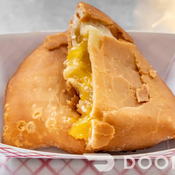 A golden-brown fried pie, split open to reveal a bright yellow fruit filling, in a paper tray.