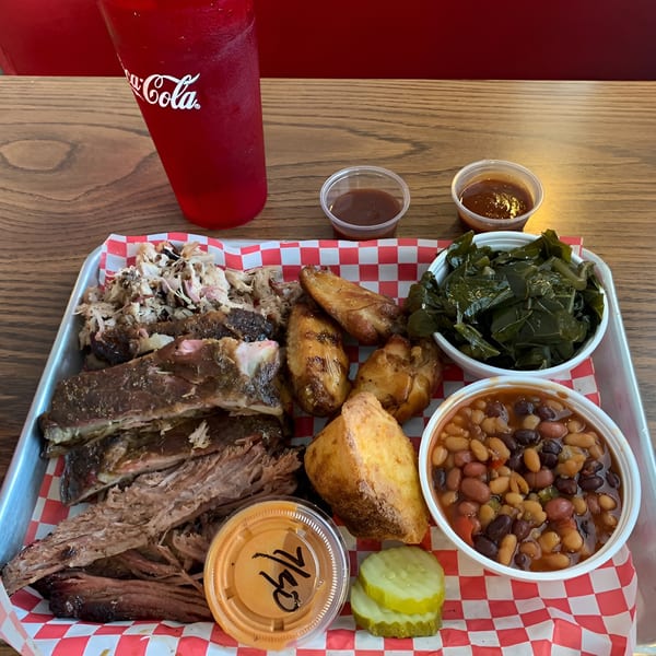 A Fire It Up BBQ platter with ribs, pulled pork, chicken wings, collard greens, baked beans, and cornbread.