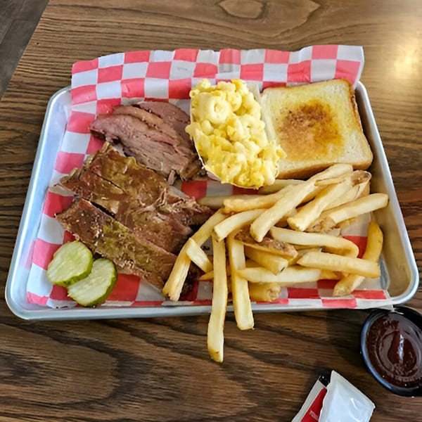 Fire It Up BBQ platter with sliced brisket, ribs, mac and cheese, fries, toast, and pickles.